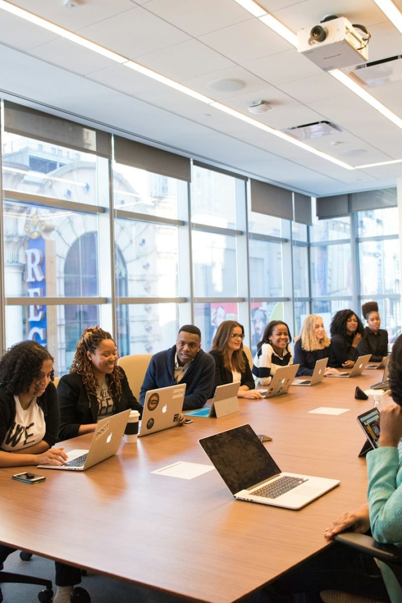 group of people sitting beside rectangular wooden table with laptops